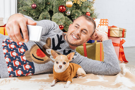 男人拿笑着的自拍与吉华狗和圣诞节树的图片