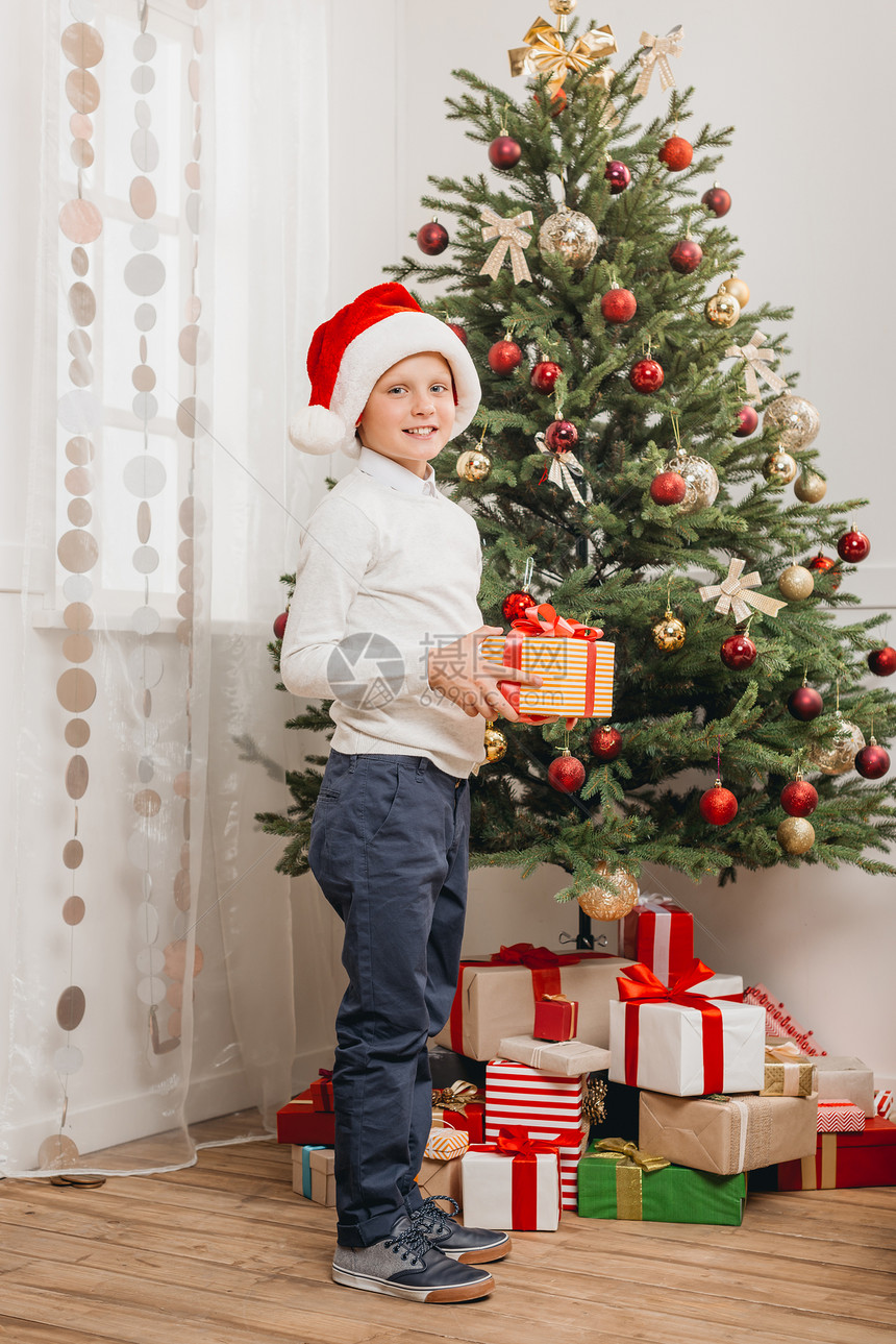 带着圣诞礼物的圣塔帽男孩在光图片