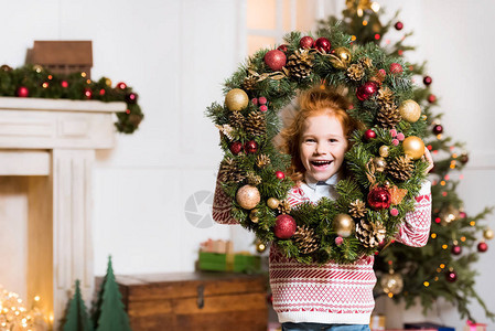 快乐的小女孩肖像与圣诞节花圈看相机图片
