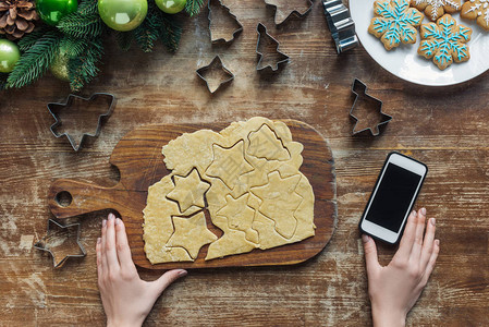 女人的局部视图带空白屏幕的智能手机和木板上的圣诞节饼图片