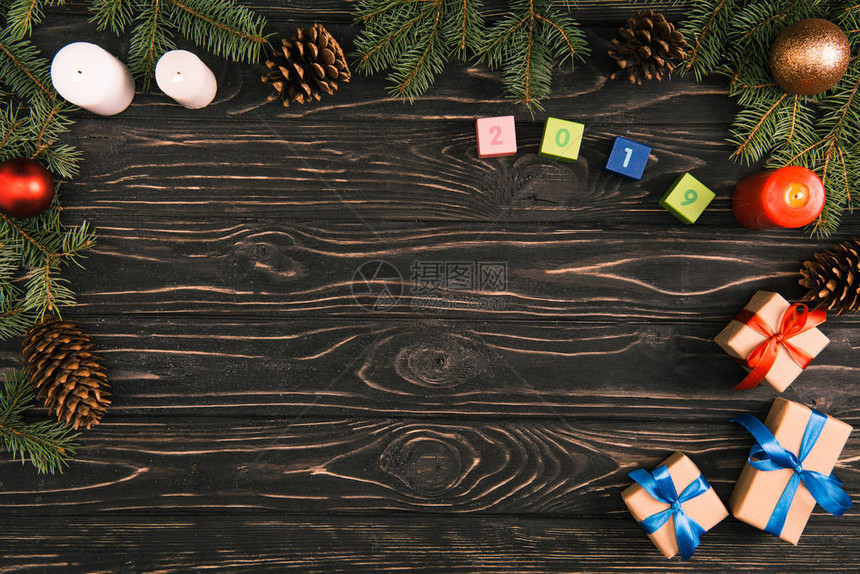 在立方体圣诞礼物蜡烛和木面上带有和松锥的圆形树枝上的2019年图片