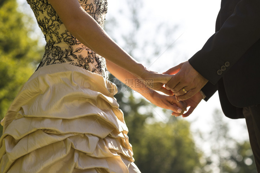 新娘和新郎在阳光明媚的日子里在户外举行婚礼誓言时彼此握着图片