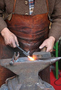 一位年长铁匠的手用锤子和铁砧打铁图片