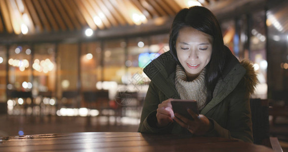 晚上使用手机的年轻妇女在夜间图片