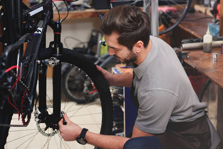 在车间修理自行车轮的围裙机修工长图片