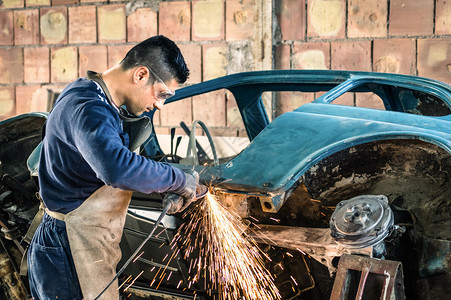 年轻机械工人在凌乱的车库里修理一辆旧的老式汽车身高清图片