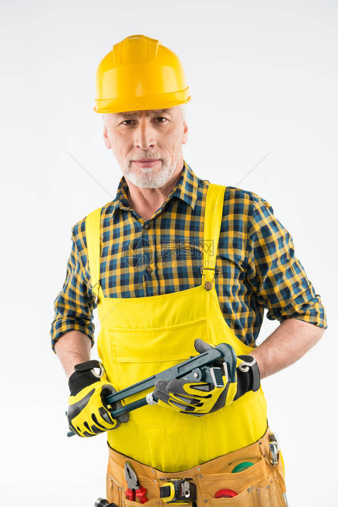 身戴硬帽的成熟工匠拿着铁管扳手看着在白色上图片