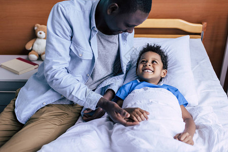 在诊所躺在床上时看着父亲的非洲男孩笑着图片
