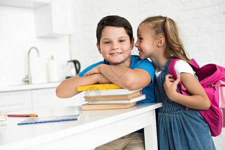桌边微笑男孩拿着书本和小妹背着包在家里附近讲图片