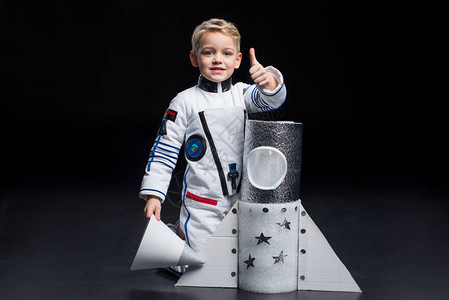 在太空服上微笑的小男孩宇航员跪在玩具飞船附图片