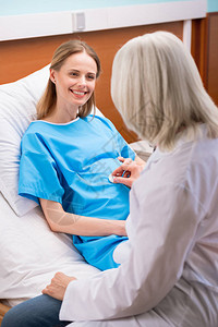 微笑的孕妇躺在病床上看着医生听未出图片