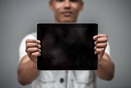 以灰色背景展示数字平板电脑的有吸引力的非裔美国人男图片