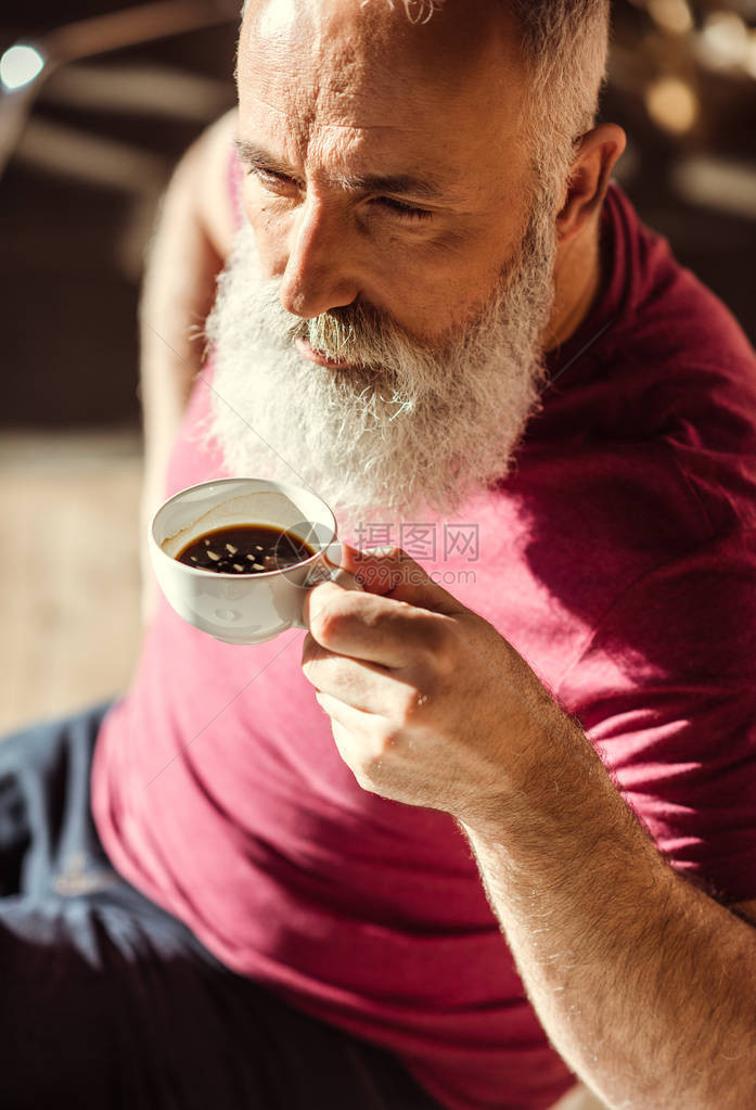 有胡子的老人拿着白杯喝咖啡图片