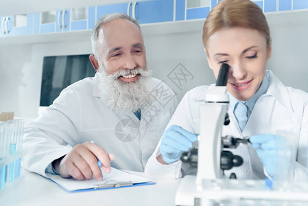两名穿着白大衣的快乐科学家在化学实验室与显背景图片