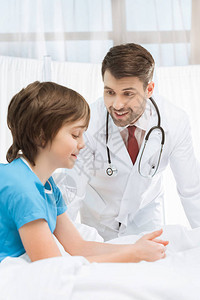 医生看着小男孩病人坐在医院的床上看图片