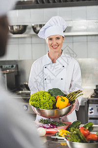 微笑的厨师拿着蔬菜碗在餐厅图片