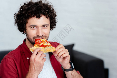 英俊的年轻人吃披萨看着相机图片