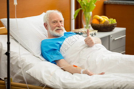 对躺在医院床上的老年病人微笑并举起图片