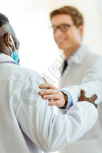 拍肩膀身穿实验室大衣的年轻医生通过拍他的肩背景
