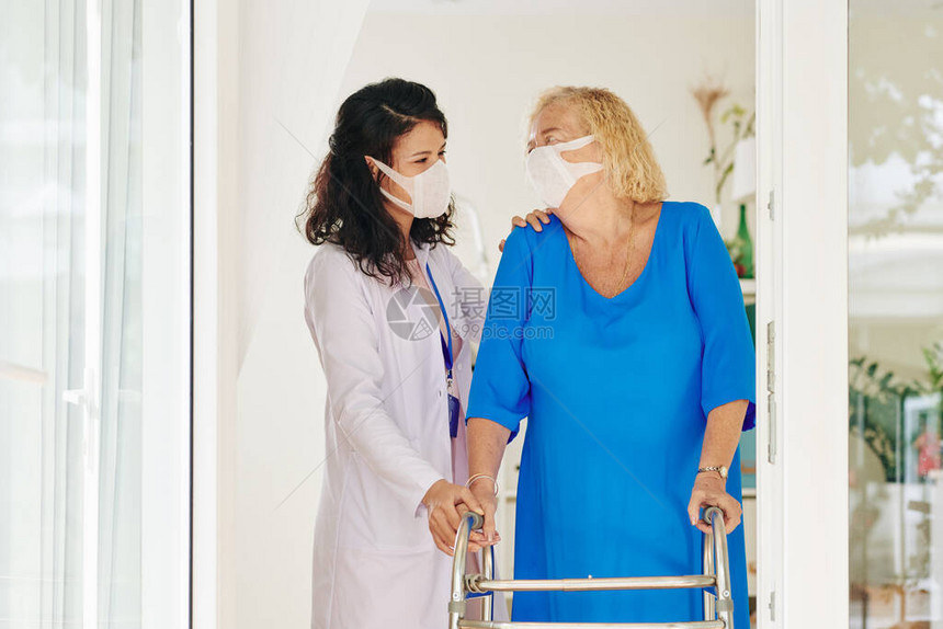 戴医用口罩的护理人员帮助老年妇女在助行器图片