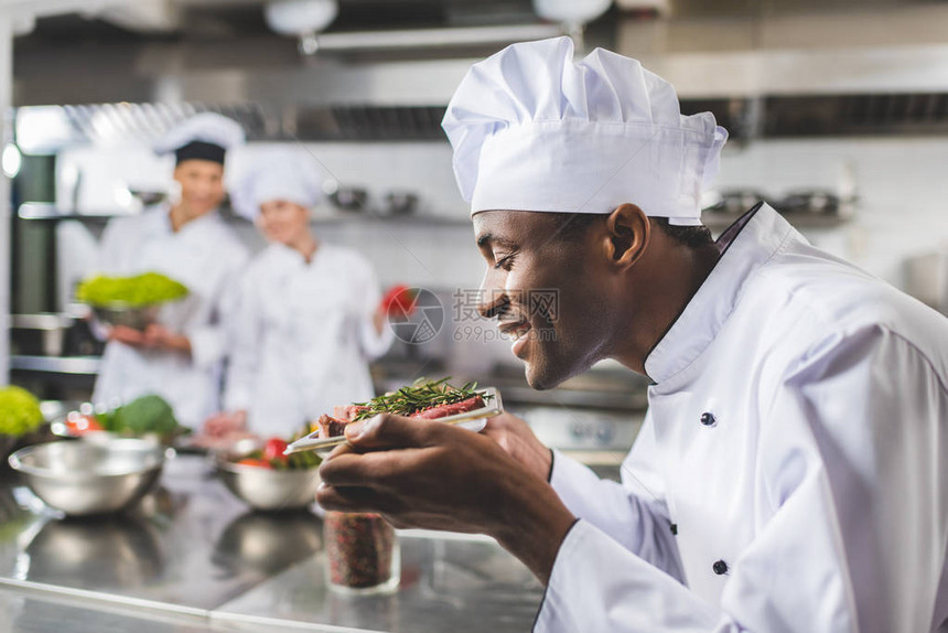 微笑的非洲裔美国厨师在餐厅厨房用香草嗅生肉图片