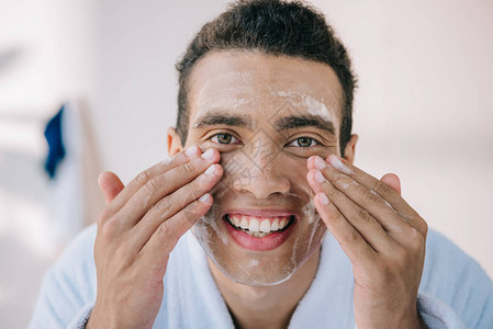 穿着浴袍的英俊年轻男子用面容泡沫洗脸图片