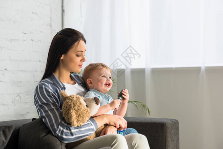年轻的母亲和微笑的婴儿小宝与泰迪熊坐在图片