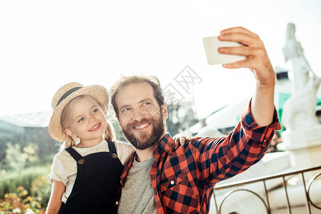 微笑的父亲用智能手机自拍和女儿一图片