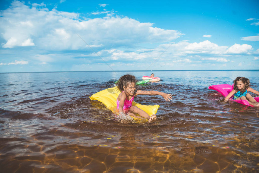 多文化的小女孩在海上用充气床垫游泳图片
