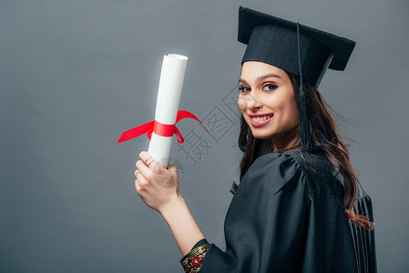 穿着学术礼服和毕业文凭上限的在灰色上被孤立图片