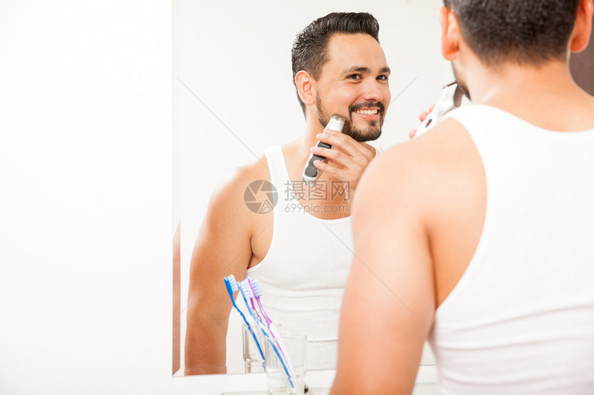 一个有吸引力的年轻人在浴室镜子前用电动剃须刀图片