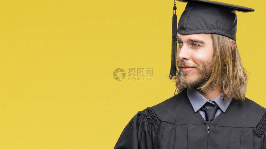 英俊的年轻毕业男子长发与孤立的背景笑着看一边看图片