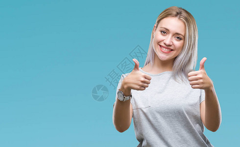 身处孤立背景的金发年轻女子赞同用手大拇指微笑和为成功而高兴图片