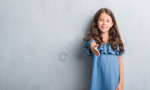 年轻的西班牙裔孩子在垃圾灰色的墙上微笑着友好地握手作为问候和欢迎图片