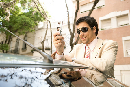 年轻的商人一边靠在树对齐街上的汽车上一图片