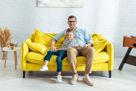 父亲和儿子在坐黄色沙发图片