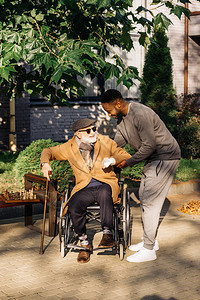 帮助老年残疾人从街上轮椅上起身的非洲男子AfricanAfricanAmerica背景图片