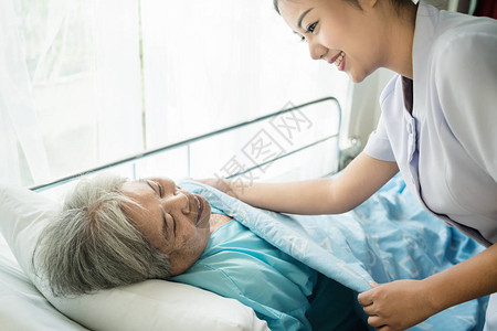 接受老年护理的亚洲护士在养老院为她盖了一图片