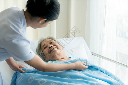 接受老年护理的亚洲护士在养老院为她盖了一图片