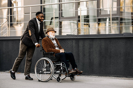 坐在轮椅上笑着微笑的老年残疾人和非洲男图片