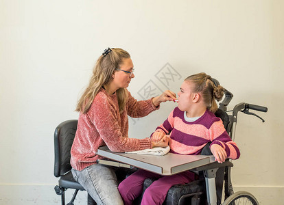 一名坐在轮椅上的残疾儿童正在接受帮助个人卫生的志愿护图片