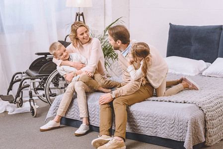 残疾父亲和幸福母亲与子女一起坐在床上图片