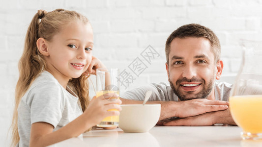 父亲和女儿喝橙汁看摄影机图片