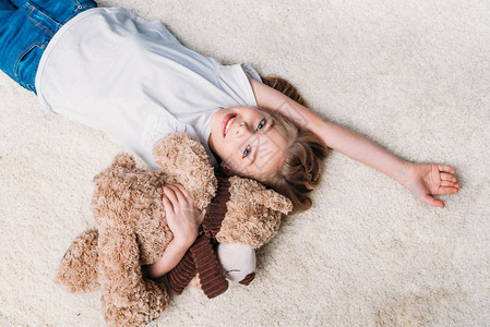 小女孩在家中躺在地毯上时抱着泰迪图片