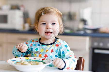 可爱的女婴从勺子蔬菜面条汤吃食物儿童喂养和发展理念可爱的蹒跚学步的女儿背景图片