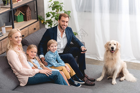 快乐的年轻家庭与狗一起坐在沙发上看相机图片