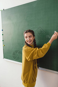 在黑板上写字的微笑高中女学生背景图片