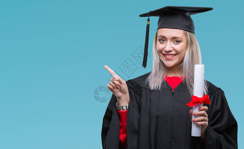 身着毕业制服的金发年轻金发女青年在孤立的背景中持有学位图片