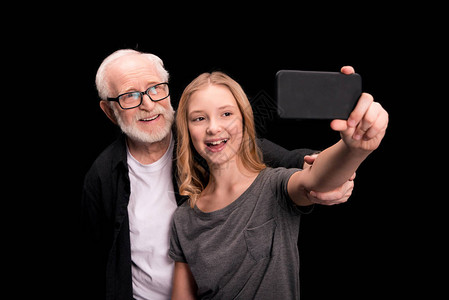 微笑的祖父和孙女带着智能手机自拍在图片