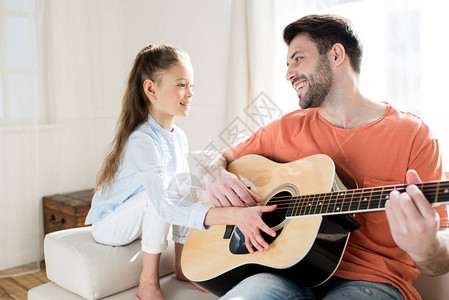 快乐的父亲和女儿弹吉他在家里看着对方图片